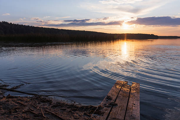 Beautiful sunset over a tranquil lake, featuring a wooden pier and peaceful water reflections. Forested background adds a natural and calming vibe, perfect for relaxation and travel inspiration