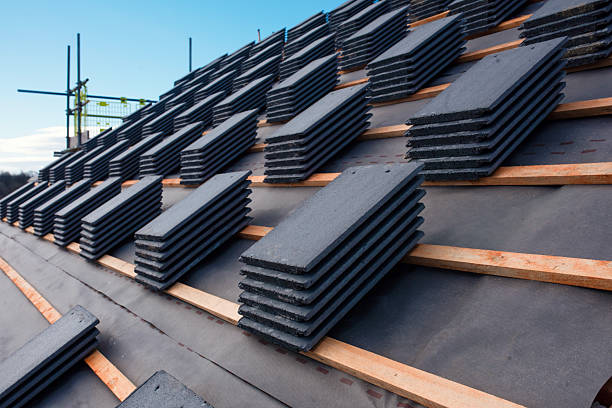 istock Construction worker carefully places roof tiles on a sloped surface while standing on top of a building under a clear blue sky, showcasing the effort involved in roofing work 2218586187