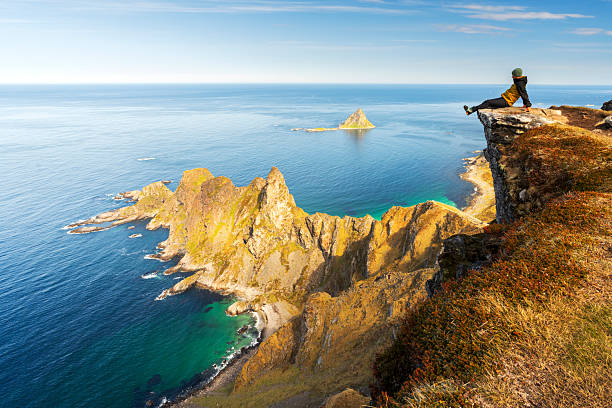Hiker sitting on rock above the ocean admiring rocky peaks in a summer day, Bleik, Andoy, Vesteralen Islands, Nordland county, Norway