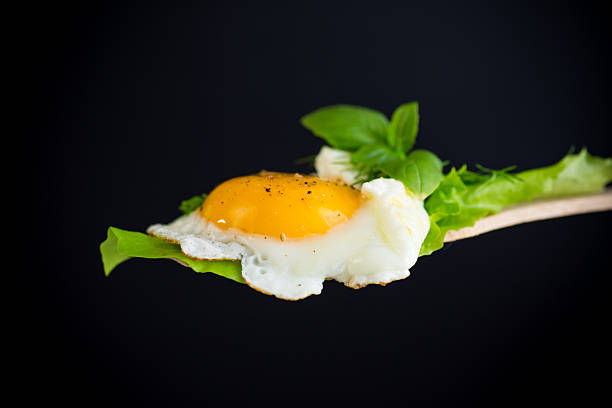 istock Fried egg with greens on a wooden spatula on a black background 2218591331