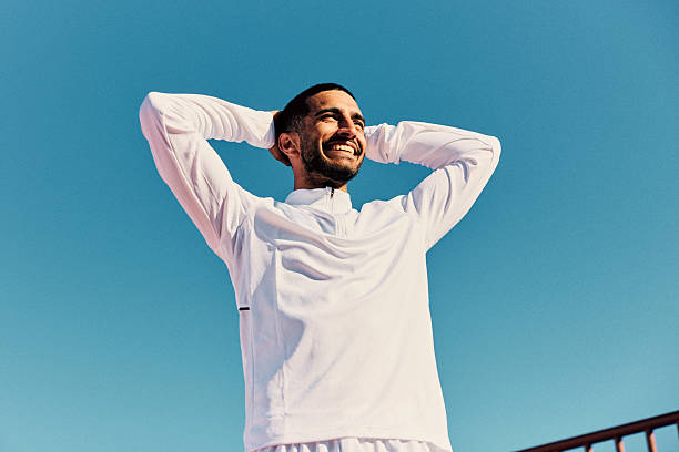 istock Cheerful young man with hands behind head, against blue sky, smiling 2218596520