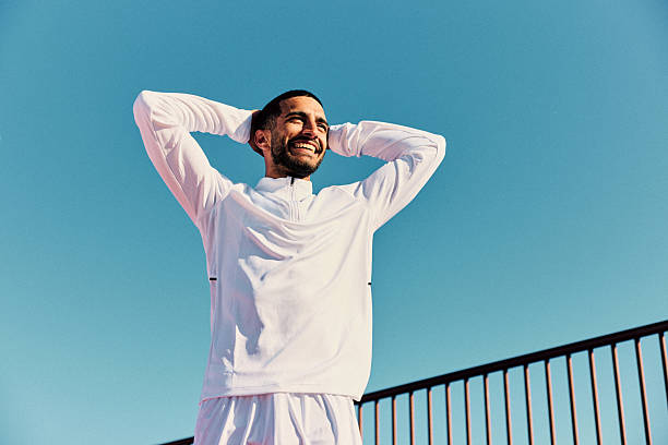 istock Cheerful young man with hands behind head, against blue sky, looking away 2218596548