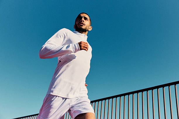 Young man wearing white active wear running outdoors with clear blue sky, looking away stock photo