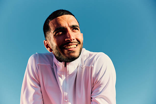 istock Young man white top looking away and smiling, against blue sky 2218596577