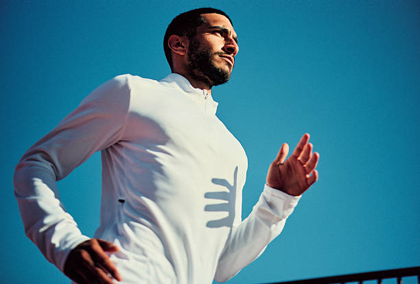 istock Young man wearing white active wear running outdoors with clear blue sky, looking away 2218596889