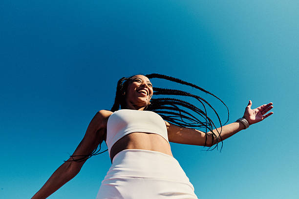 Low angle portrait of woman in her 20s with long braided hair against clear blue sky stock photo