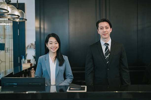 istock 2 Asian Hotel Receptionists in Formal Uniform Standing at Front Desk looking at camera smiling 2218597670