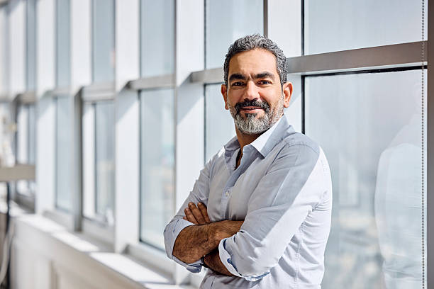 istock Smiling businessman with arms crossed leaning on window 2218600120
