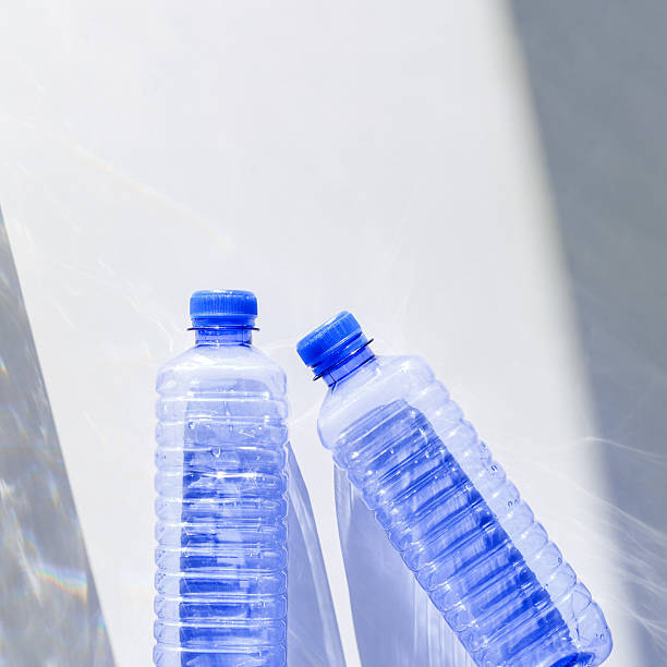 istock Blue plastic water bottles on white blue background with sunlight shadow and sun flare, Minimal top view photo, themes of ecology, recycling, sustainable living, reduce disposable plastics 2218601394