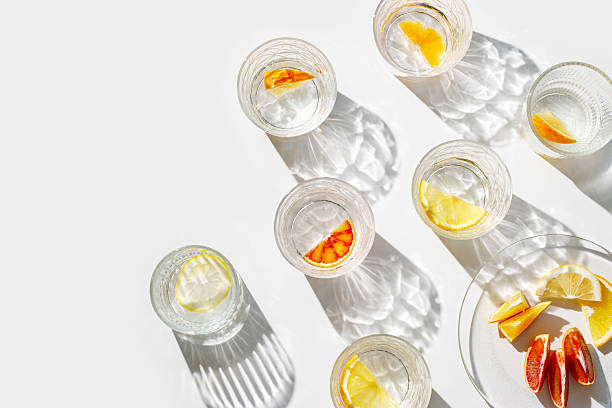 istock Fruit Infused Water in Glasses and plate with Shadows at sunlight on White background. Aesthetic Top view summer detox drink with slices of lemon and orange with sun flare from glass cups 2218603840