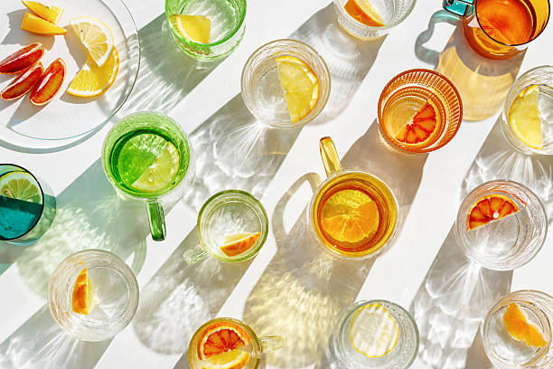 istock Colored Glasses and plate as summer still life with shadow and sunlight reflection on table, colorful glass cups of infused fruit water, slises of lemon, orange, tangerine, healthy summer drink 2218603970