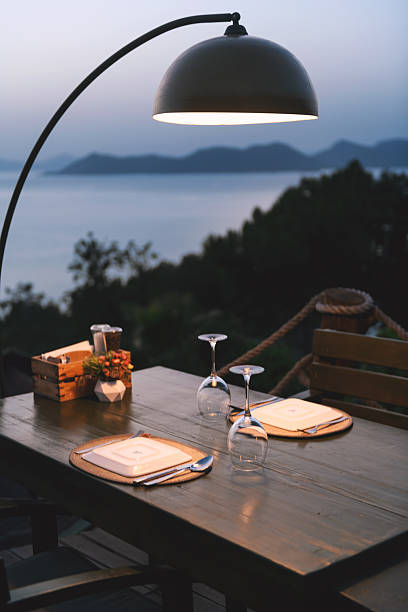 An artistic shot of an empty restaurant table with overturned plates and wine glasses against a stunning ocean backdrop stock photo