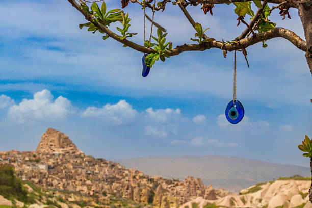 Landscape with blue Evil Eye pendants in Wish tree against blurred background of Uchisar castle in Cappadocia, Turkey. Selective focus
