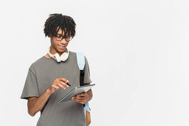 istock Young teen boy guy IT student in casual backpack bag using holding working digital tablet pad touchscreen look at camera isolated on white background. High school university college concept copy space 2218610299