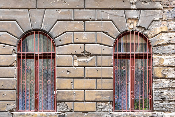 Textured background of old brickwork with bullet and shell marks from the war and two arched windows with bars