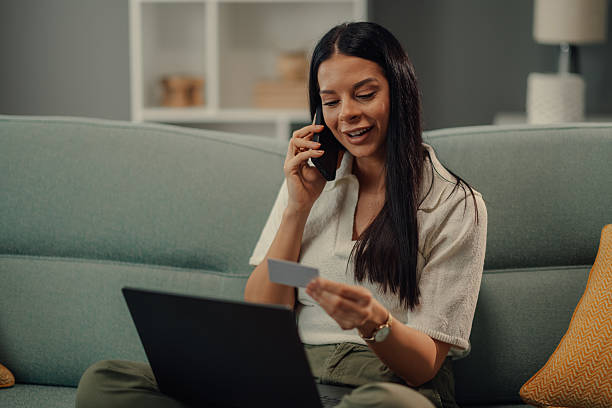 istock Young woman making online payment while talking on phone at home 2218611522