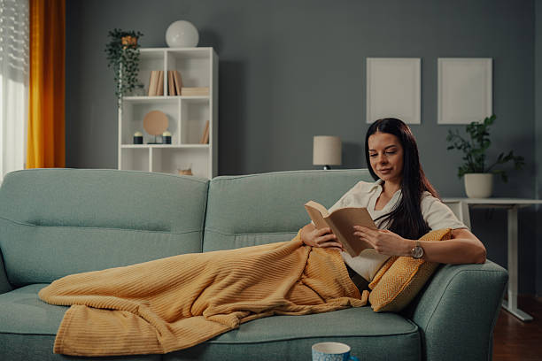 istock Young woman relaxing on sofa reading a book at home 2218612084