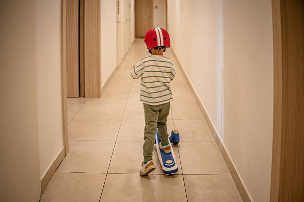 A boy scoots along the hallway inside an apartment building.