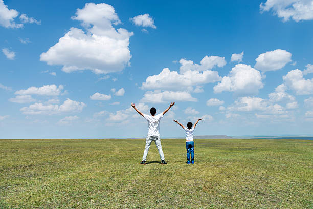 istock Father and son standing in meadow with arms outstretched 2218623585