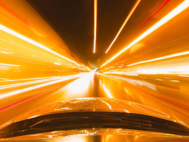 Fast car racing down a wet road at night, creating vibrant orange light trails and dynamic motion blur in an urban setting
