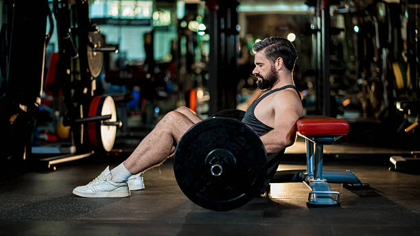 istock Strong man in black tank top preparing for hip thrust exercise with barbell on bench in gym, focused on glute and lower body training with proper form 2218631608