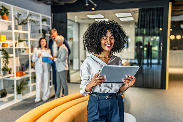 istock Smiling businesswoman using digital tablet in modern office lobby with colleagues working in background 2218632313