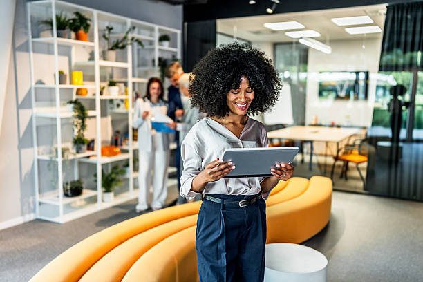 istock Smiling businesswoman using digital tablet in modern office lobby with colleagues working in background 2218632341