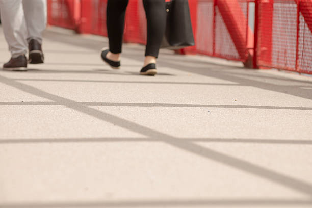The foot traffic observed on a lively pedestrian walkway, which is situated beneath a vibrant red railing structure, offers a glimpse into the dynamic urban environment filled with life