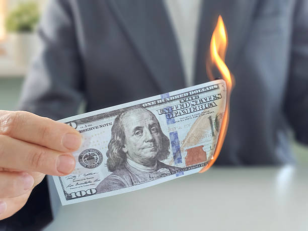 Money burning in a person's hand while wearing a suit with a blurred background