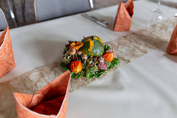 Decorative gourd centerpiece on white table with folded napkins and soft sunlight.