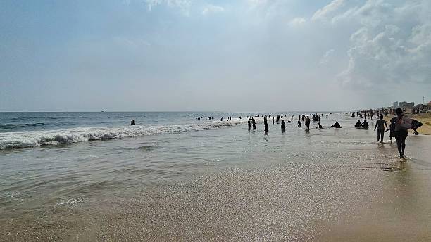 istock Crowded beach scene with people enjoying the ocean waves under a partly cloudy sky. 2218638937