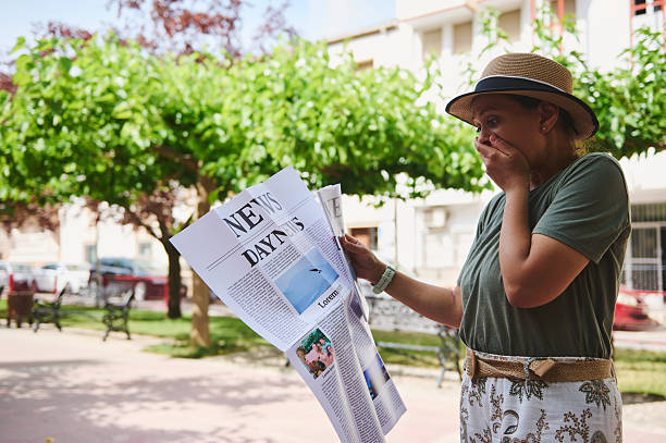 A surprised woman reacts while reading news in a newspaper at a park filled with trees and sunshine. She wears a stylish hat and casual attire.