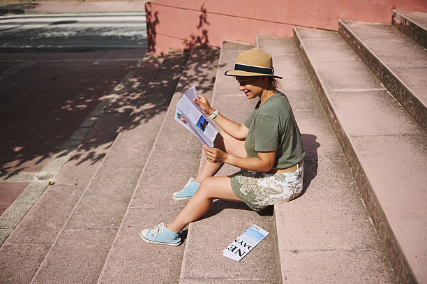 Young Woman Enjoying Leisurely Reading While Sitting Outdoors on Steps in Sunny Weather