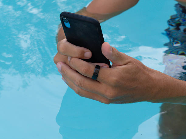 istock Hands in pool water wearing black smart ring health tracker and using smartphone. 2218651836