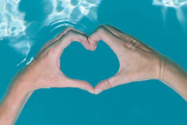 istock Hands creating a heart shape underwater in a clear swimming pool surrounded by sunlight reflecting off the surface. 2218651837
