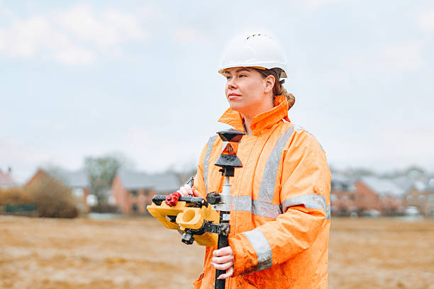 istock Female Construction surveyor using surveying equipment on building site while wearing bright reflective safety gear 2218652455