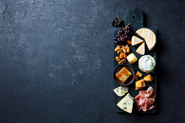istock Assortment of cheese with jamon, fresh grape and nuts on marble cutting board. Dark grey background. Copy space. Top view. 2218652551