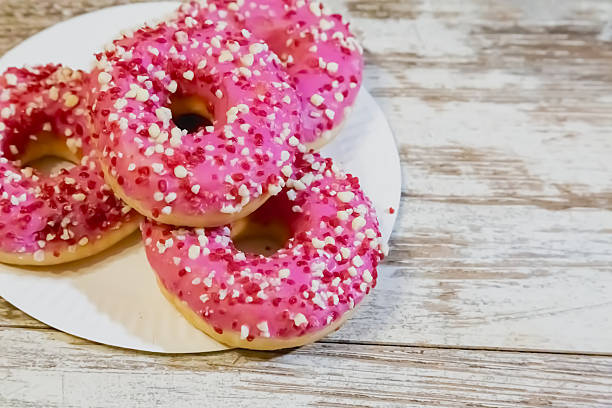 istock Doughnuts with pink glaze and sprinkles on a white plate on an old kitchen table. 2218653045
