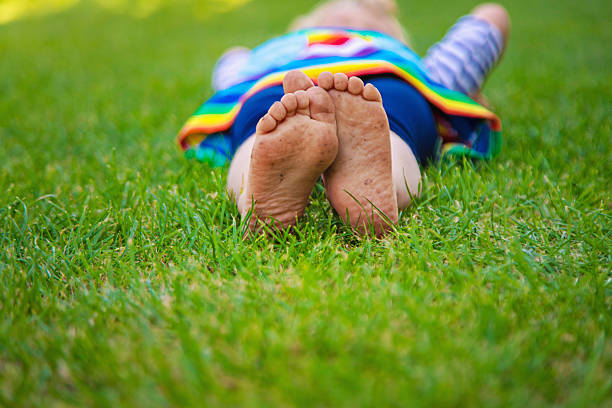 From above of anonymous kid with tender and delicate barefoot while sitting alone on green grass in park and in daylight