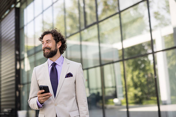 istock Smiling businessman walking and using smartphone in front of office building 2218655713