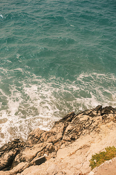 Gentle waves caressing rocky shores under a bright sun, creating a serene and picturesque coastal scene filled with tranquility