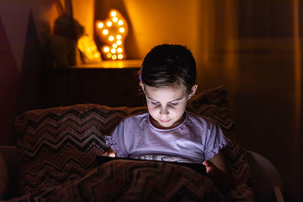 istock Little Girl Smiling While Watching a Tablet in Bed at Night 2218659532