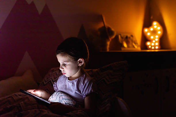 istock Little Girl Smiling While Watching a Tablet in Bed at Night 2218659573
