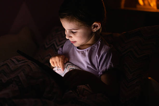 istock Little Girl Smiling While Watching a Tablet in Bed at Night 2218659594