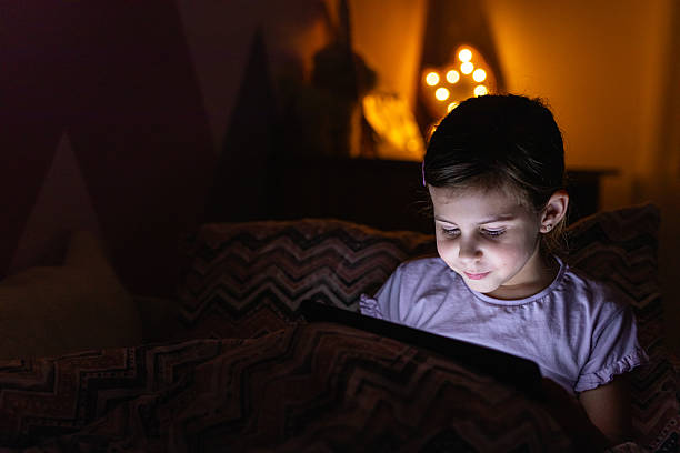 istock Little Girl Smiling While Watching a Tablet in Bed at Night 2218659623