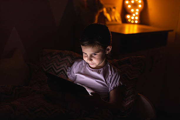 istock Little Girl Smiling While Watching a Tablet in Bed at Night 2218659647
