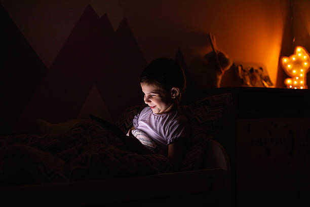 istock Little Girl Smiling While Watching a Tablet in Bed at Night 2218659652