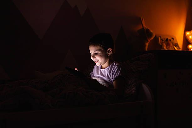 istock Little Girl Smiling While Watching a Tablet in Bed at Night 2218659669