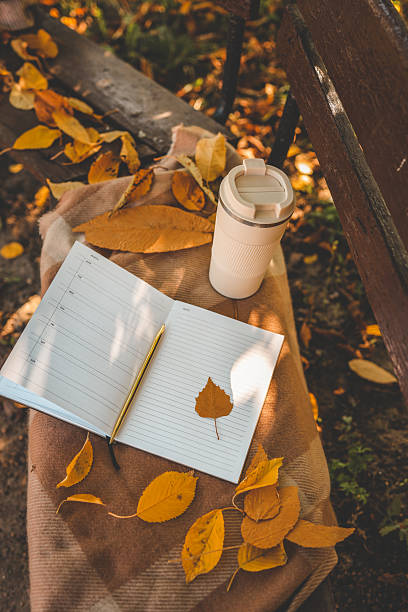 istock Open planner with gold pen and autumn leaf on lined pages, surrounded by colorful fall leaves and warm blanket fabric in natural sunlight 2218659935