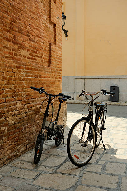 Folding bike and traditional bicycle parked on a cobblestone street in a historic city center, near an old brick wall